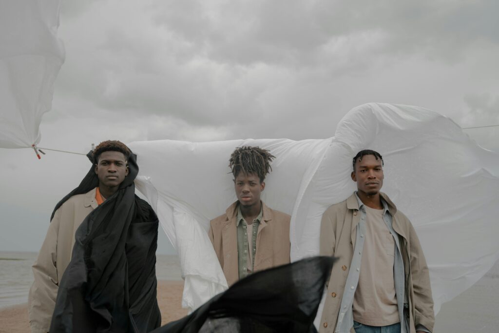 Three men standing outdoors with cloths blowing in the wind, showcasing fashion and expression.